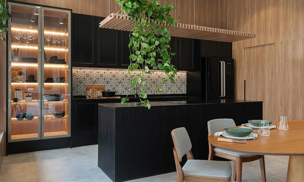Cozinha preta com ilha, cristaleira iluminada e mesa de jantar